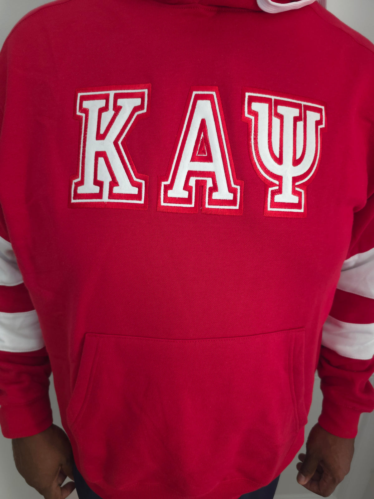 A red hooded sweatshirt with white and red Greek letters 'KAΨ' across the chest. Detailed view of high-density satin stitch embroidery on red Kappa Alpha Psi hooded sweatshirt