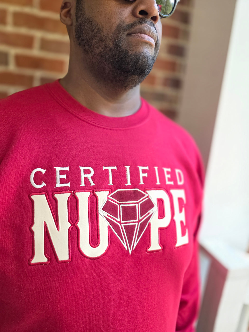 Detailed view of high-density satin stitch Certified Nupe embroidery on crimson fleece crewneck
