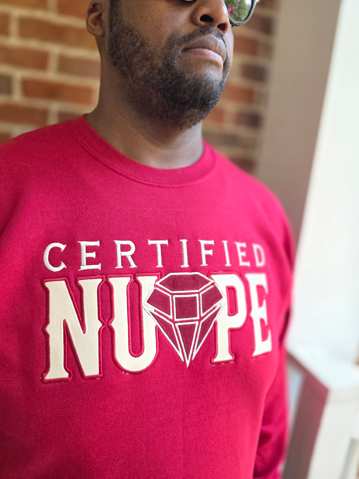 Detailed view of high-density satin stitch Certified Nupe embroidery on crimson fleece crewneck