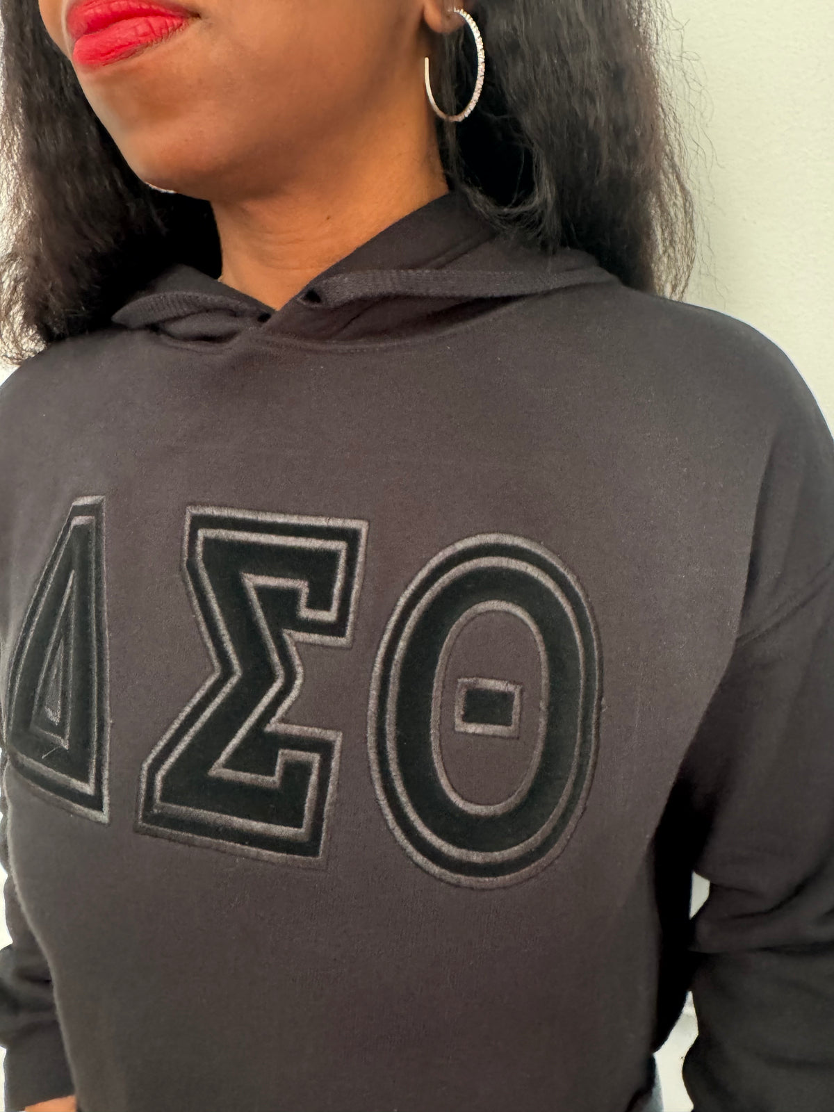 Close-up view of raised black satin stitch embroidery on black fleece crop hoodie. Delta Sigma Theta black-on-black cropped hoodie.